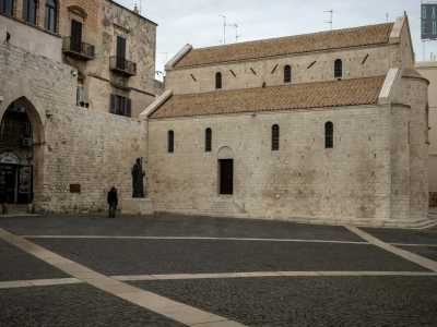 Il profilo delle fiancate a doppio ordine, interrotte solo dalle sette finestrelle, si staglia silenzioso al fianco della bronzea statua del santo patrono di Bari